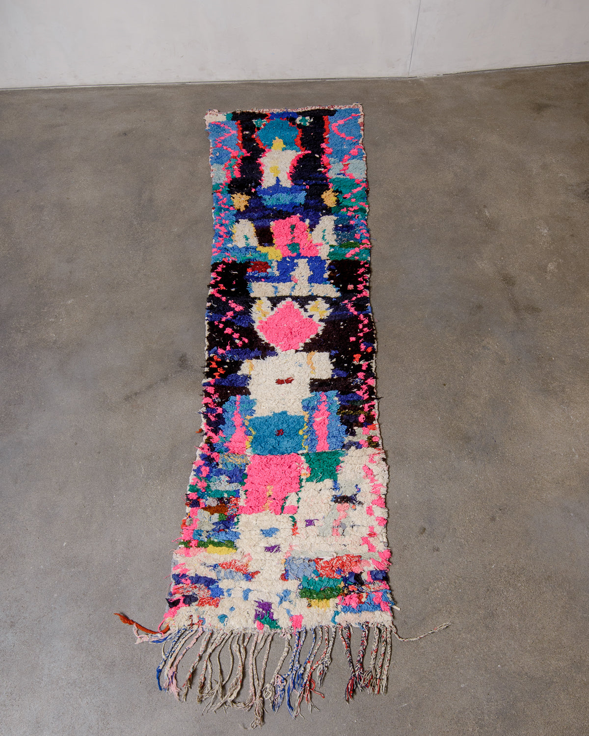 Berberlin boucherouite runner rug featuring blue, black and pink, laying flat on a concrete floor.